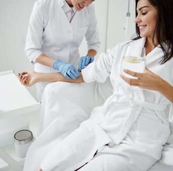 Cropped portrait of beautiful woman in white bathrobe sitting in armchair and receiving IV infusion.